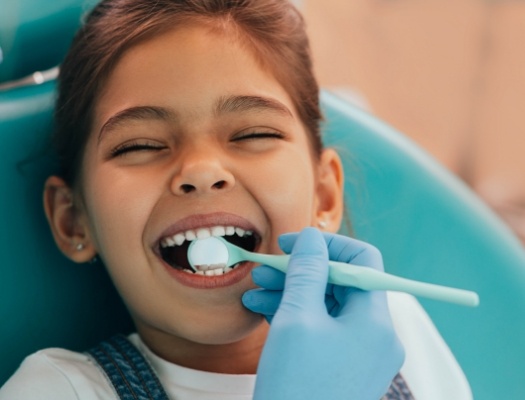 Child in dental chair smiling while teeth are examined