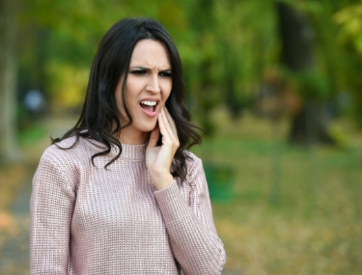 Woman in sweater walking outside rubbing tooth in pain